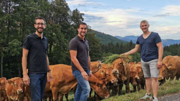 Die Gründer von DeinDorfleben stehen mit einem Bauern im Schwarzwald vor einer Kuhweide