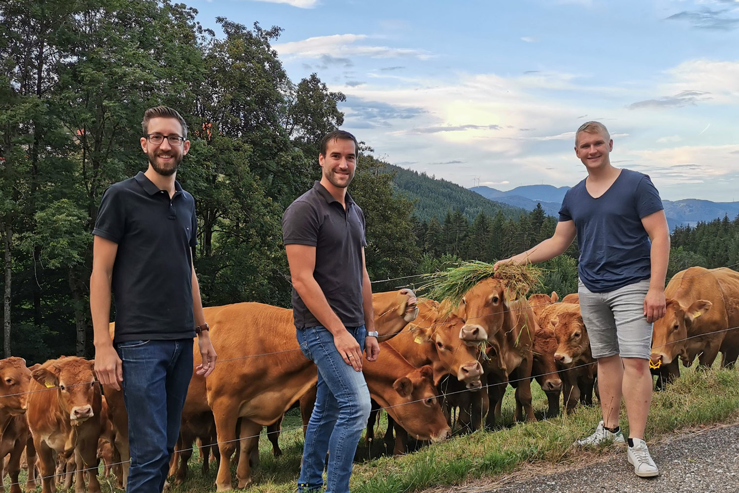 Die Gründer von DeinDorfleben stehen mit einem Bauern im Schwarzwald vor einer Kuhweide