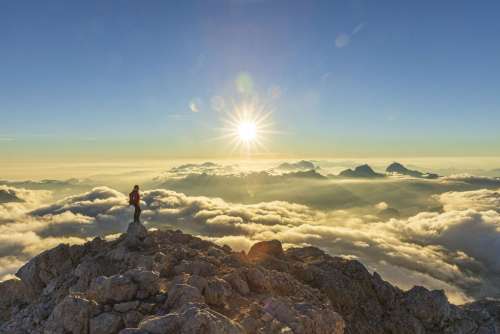 Ulla Lohmannsteht auf einem Berg in den Alpen über den Wolken, die Sonne scheint, es ist in Sonnenstern zu sehen